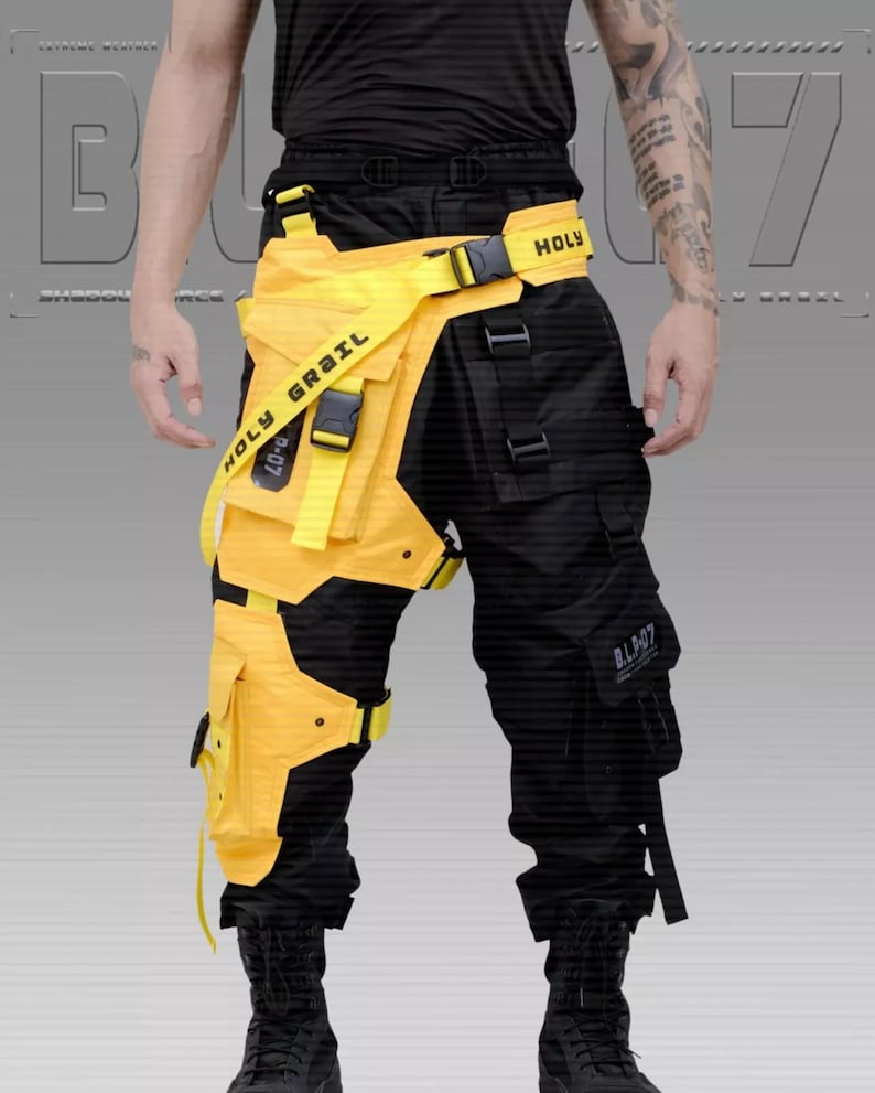 Puede incluir: Pantalones cargo negros con cintur&oacute;n utilitario y accesorios para las piernas amarillos. El cintur&oacute;n y los accesorios para las piernas tienen el texto "HOLY GRAIL" y "B.L.907". Los pantalones tienen m&uacute;ltiples bolsillos y correas. El dise&ntilde;o es futurista y t&aacute;ctico.