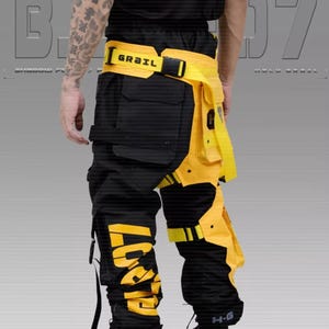 Puede incluir: Pantalones cargo negros y amarillos con m&uacute;ltiples bolsillos y correas. Los pantalones presentan letras amarillas grandes en la pierna izquierda y un cintur&oacute;n amarillo con la palabra "GRAIL". El dise&ntilde;o es moderno y funcional.