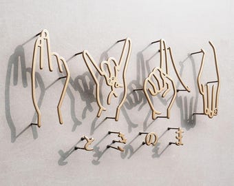 May include: Wall decor featuring hand gestures spelling out a word, with additional Japanese characters below. The hands are made of a light-colored material, casting shadows on the gray wall. The overall design is minimalist and artistic.