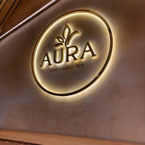 May include: Aura Wellness Spa sign. The sign is circular with a gold border and a glowing light. The word "AURA" is in gold letters, with a leaf design above it. Below the word "AURA" is the text "WELLNESS SPA".