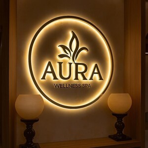 May include: Illuminated sign for "Aura Wellness Spa" with a circular design and a leaf-like emblem. The sign is lit with a warm, inviting glow. Two decorative candle holders with spherical shades flank the sign.