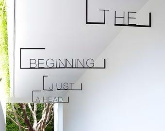 May include: Black metal wall art featuring the text THE BEGINNING JUST AHEAD, with each word framed by thin, angular black lines. The letters are sans-serif and uppercase, mounted on a white wall surface, creating a clean, linear aesthetic.