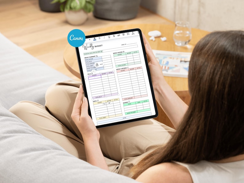 May include: A black tablet displaying a "Weekly Budget" template from Canva. The template features sections for income, expenses, and goals, with color-coded categories. The tablet is held by a person.