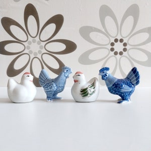May include: Four ceramic chicken figurines. One is white, and three are blue and white. The blue and white chickens have green and red accents.
