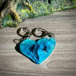 Op de afbeelding: Tweedelige hartvormige sleutelhangers. Elke helft is een doorschijnend blauw met een zwart silhouet van een zeedier. De sleutelhangers hebben zilverkleurige metalen sluitingen.