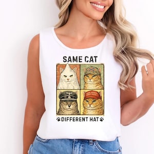 May include: White tank top featuring a graphic of four cats, each wearing a different hat. The text "SAME CAT" is above the images, and "DIFFERENT HAT" is below. The cats are in a square grid.