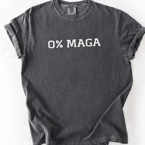 May include: Dark gray t-shirt with the text "0% MAGA" printed in white. The shirt has a crew neck and short sleeves. The fabric appears to be pre-washed for a vintage look.