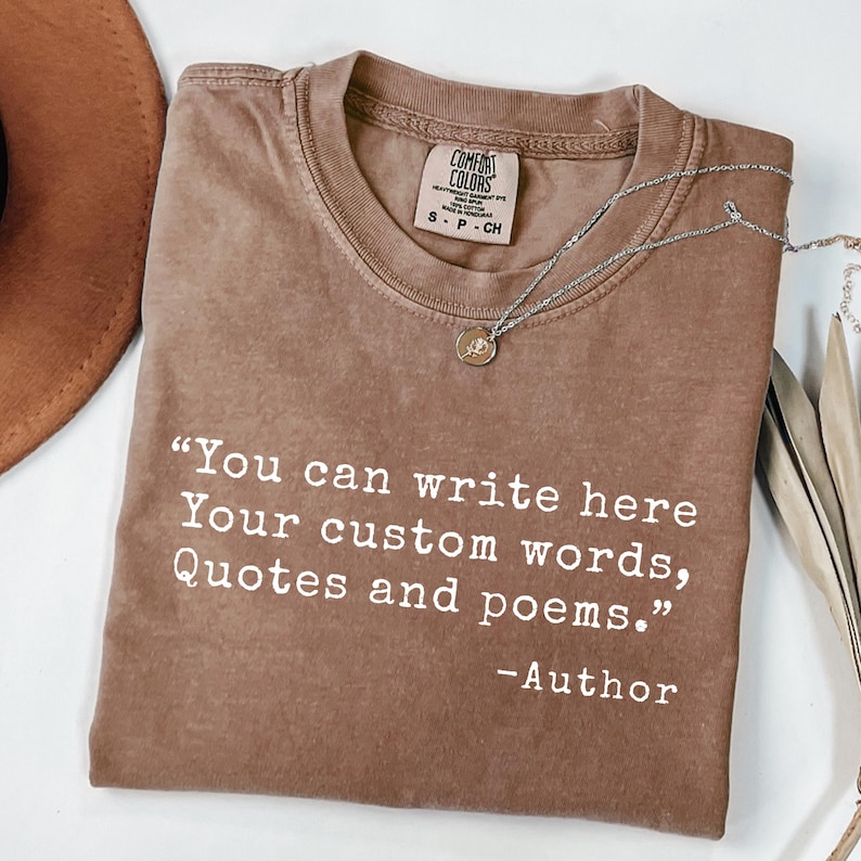 May include: A brown Comfort Colors t-shirt with the text "You can write here Your custom words, Quotes and poems." and "-Author" in white. A silver necklace with a pendant is draped across the shirt.