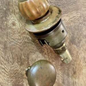 May include: A brass door knob set featuring one fluted, spherical knob attached to a cylindrical mechanism and a second, smooth, plain spherical knob. Both components exhibit a weathered, metallic finish with visible signs of age and patina.
