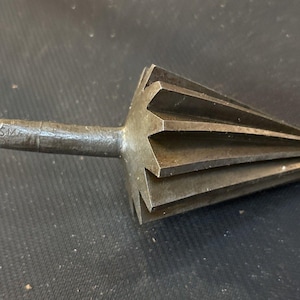 May include: A dark gray metal reamer tool featuring a conical head with multiple sharp, longitudinal fluted cutting edges and a cylindrical shank. The shank is marked with the letters SM, indicating a specific tool size or manufacturer identification.