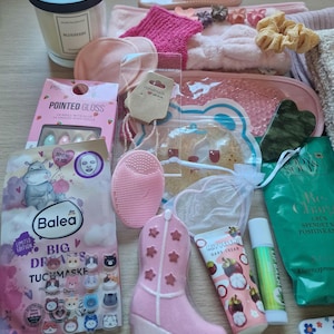 K&ouml;nnte beinhalten: Eine Auswahl an Beauty- und Pflegeprodukten, darunter eine Kerze, Gesichtsmasken, ein Nagelset, ein rosa Cowboy-Stiefel und verschiedene Hautpflegeartikel. Die Artikel sind auf einer hellen Oberfl&auml;che angeordnet.