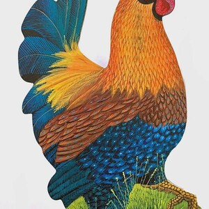 May include: A flat, cutout-style rooster figure featuring a vibrant colour palette of orange, yellow, blue, and red. The rooster stands on a green grassy base, with detailed feather textures and a prominent red comb and wattle on its head.
