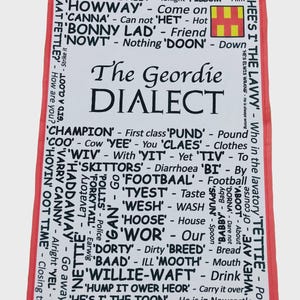 May include: A white rectangular tea towel with a red border featuring a black printed list of Geordie dialect words and their definitions. The text includes phrases like The Geordie DIALECT, GID A GOOD TWANK, and WHEES I THE LAVVY, along with a small yellow and red flag graphic.