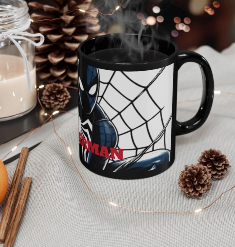 May include: Black ceramic mug featuring a Spider-Man graphic. The design includes a black and blue Spider-Man figure with a white spider web background and the word "SPIDERMAN" in red. The mug has a black interior and handle.