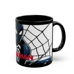 May include: Black ceramic mug featuring a Spiderman design. The mug has a black handle and interior. The Spiderman graphic includes a black and blue Spiderman with a white spiderweb background and the word "Spiderman" in red.