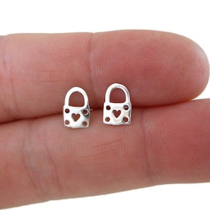 May include: A pair of silver padlock earrings with a small heart cutout in the center of each padlock.
