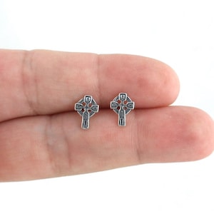 May include: A pair of silver Celtic cross stud earrings. The earrings are small and delicate, and they feature a detailed design.