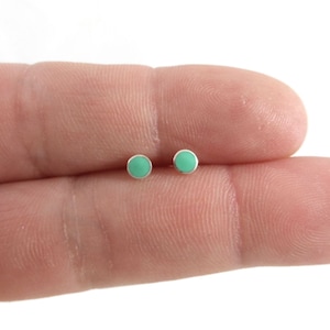 May include: A pair of small, round, turquoise stud earrings. The earrings are made of silver and have a simple, minimalist design.