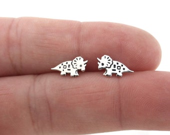 May include: A pair of silver-toned earrings featuring a small, detailed triceratops dinosaur design.