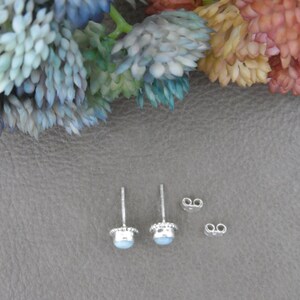 May include: A pair of silver stud earrings with light blue gemstones. The earrings are shown on a grey surface with two extra earring backs.