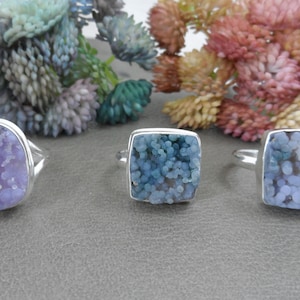 May include: Three silver rings with different shaped settings featuring blue and purple agate stones.