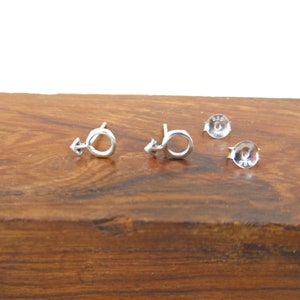 May include: A pair of silver earrings with a male symbol design. The earrings are on a wooden surface.
