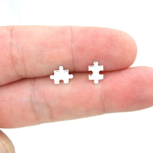 May include: A pair of silver puzzle piece stud earrings. The earrings are small and delicate, and they are perfect for everyday wear.