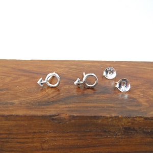 May include: A pair of silver earrings with a male symbol design. The earrings are on a wooden surface.