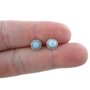 May include: A pair of silver stud earrings with a light blue gemstone centre and a beaded border.