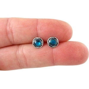May include: A pair of silver stud earrings with a blue gemstone in the center of each earring. The earrings have a decorative border around the gemstone.