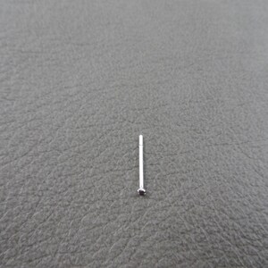 May include: A silver nose ring with a small, dark red gemstone.