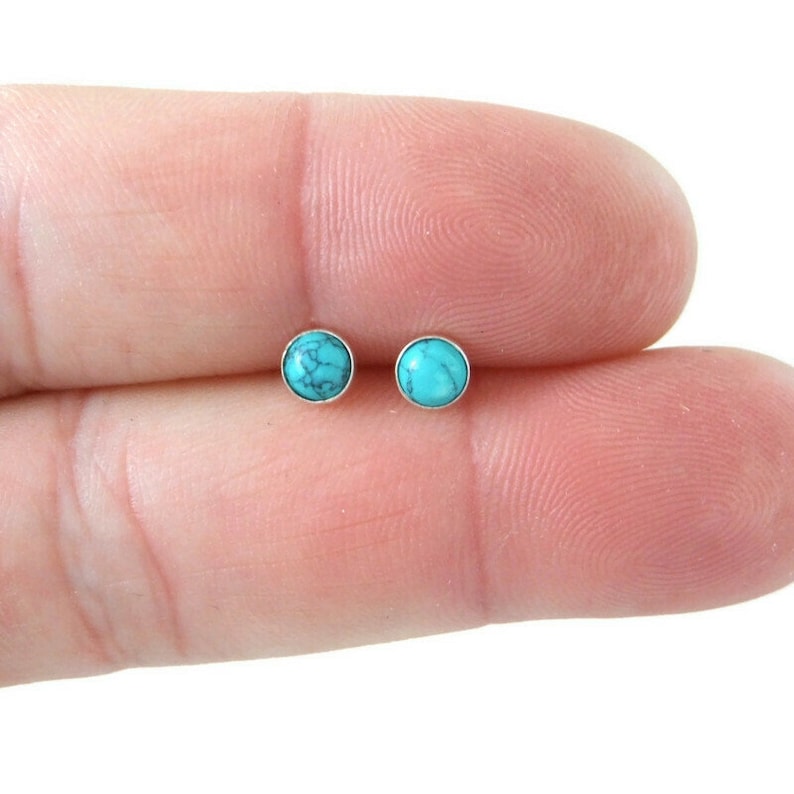 May include: A pair of silver stud earrings with turquoise stones. The stones are round and have a light blue color.