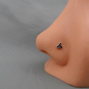 Pode incluir: Um piercing de nariz de prata com um design de nó celta. O piercing está no nariz de um manequim.