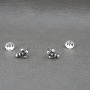 May include: A pair of silver stud earrings with a cluster of small round beads in the shape of a flower.