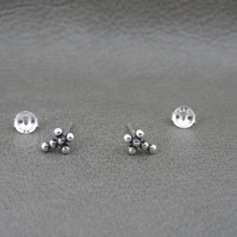 May include: A pair of silver stud earrings with a cluster of small round beads in the shape of a flower.