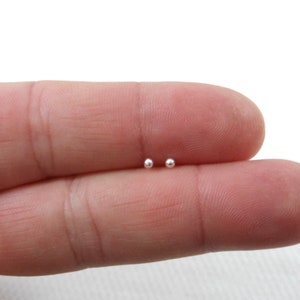 May include: A pair of small, silver ball stud earrings. The earrings are shown on a finger.