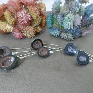 Op de afbeelding: Een paar oorbellen met zilveren haakjes en geode-steentjes. De stenen zijn een mix van zwart, bruin en wit met een kristal-achtige textuur.