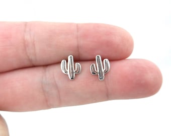 May include: A pair of silver cactus stud earrings. The earrings are small and delicate, and they feature a simple cactus design.