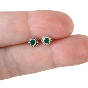 May include: A pair of silver stud earrings with small green gemstone accents.