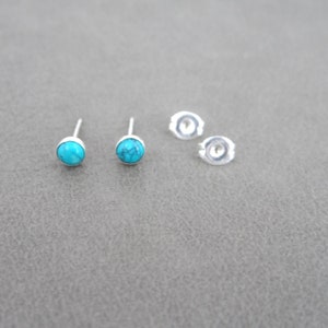 May include: A pair of silver stud earrings with turquoise stones. The earrings are shown on a gray surface.