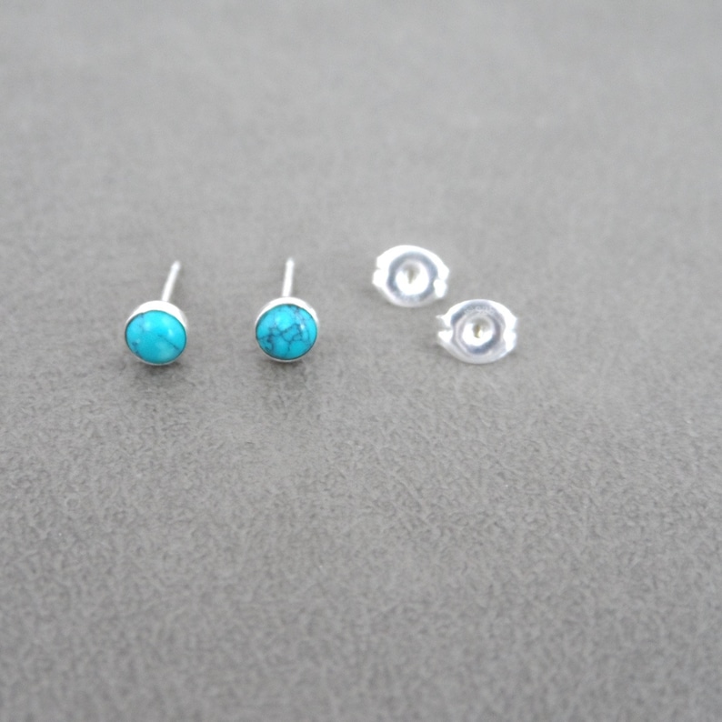 May include: A pair of silver stud earrings with turquoise stones. The earrings are shown on a gray surface.