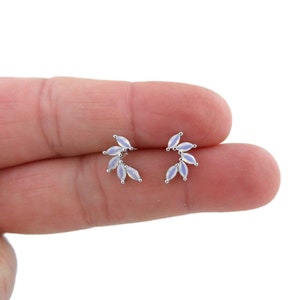 May include: A pair of silver earrings with a delicate design featuring a cluster of small, white opal-like stones arranged in a leaf shape.