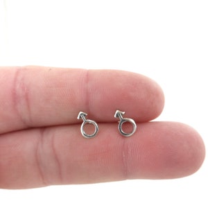 May include: A pair of silver stud earrings with a male symbol design.