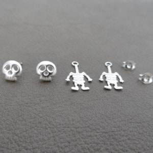 May include: A set of six silver earrings featuring two skull designs and two skeleton designs. The set also includes two earring backs.