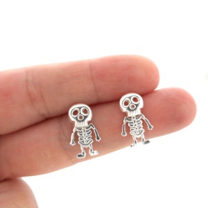May include: A pair of silver skeleton earrings. Each earring features a small, detailed skeleton with a skull head.