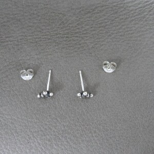 May include: A pair of silver stud earrings with a cluster of small silver beads. The earrings are on a gray surface.