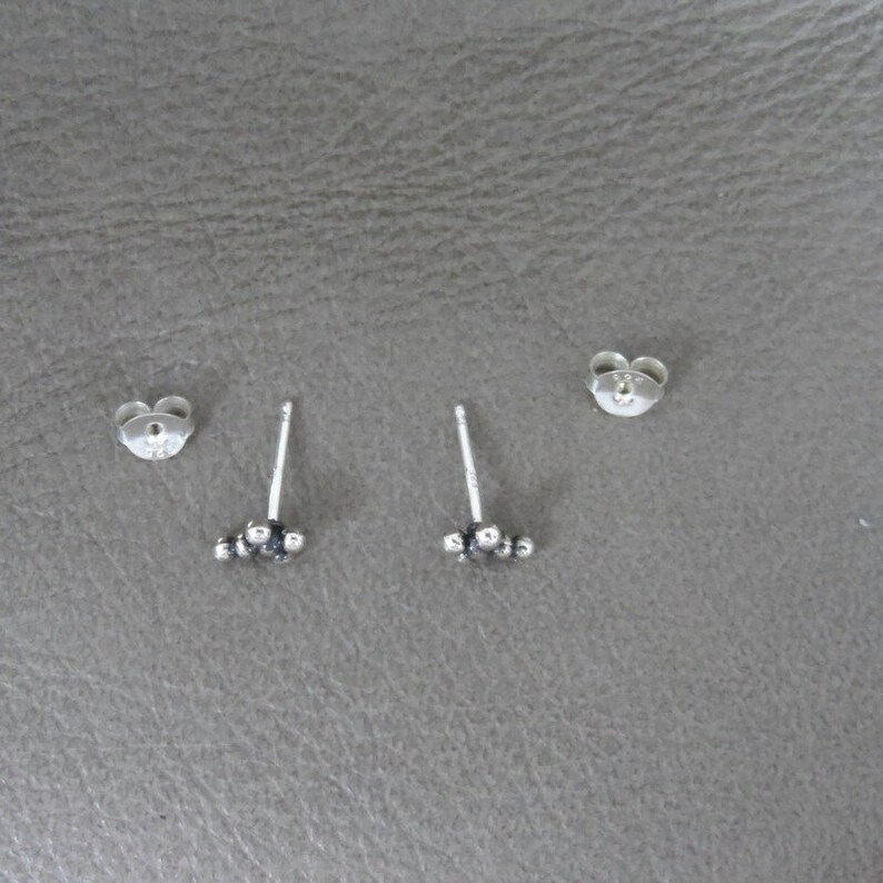May include: A pair of silver stud earrings with a cluster of small silver beads. The earrings are on a gray surface.
