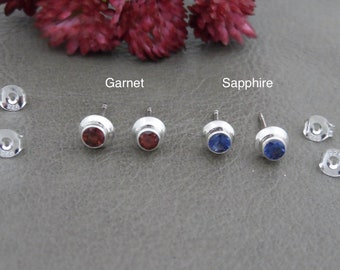Puede incluir: Dos pares de pendientes de plata con piedras preciosas de granate rojo y zafiro azul. Los pendientes se muestran sobre una superficie gris con las palabras "Granate" y "Zafiro" impresas encima.