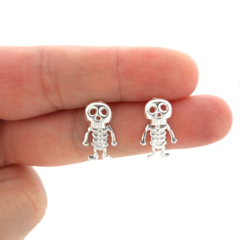 May include: A pair of silver skeleton earrings with a skull design. The earrings are small and delicate, and they would make a great gift for a friend or loved one.
