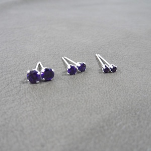 May include: Three pairs of silver stud earrings with purple gemstones. The earrings are arranged in a row from smallest to largest.